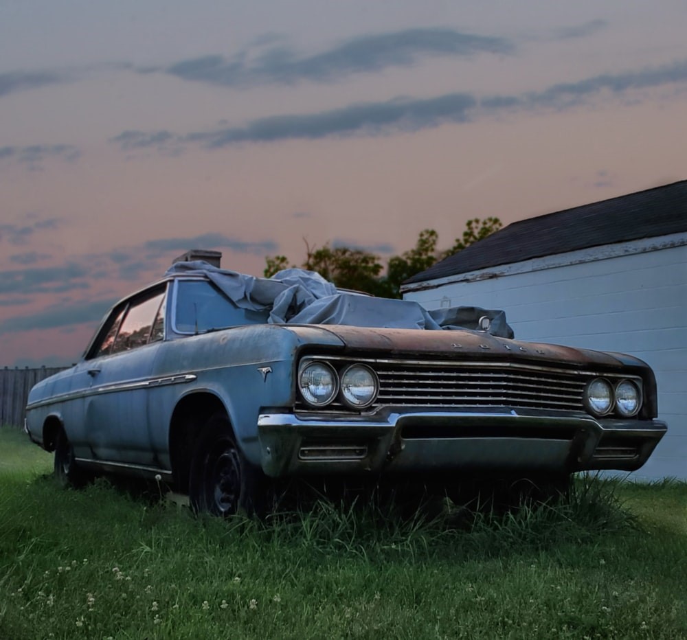 A blue, old junk car parked in the backyard.