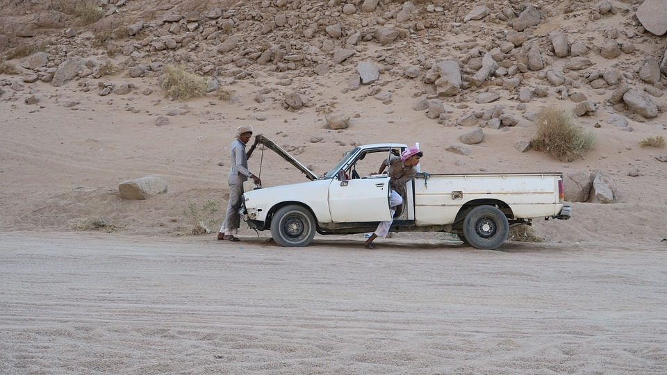 A man repairing his car near a mountain