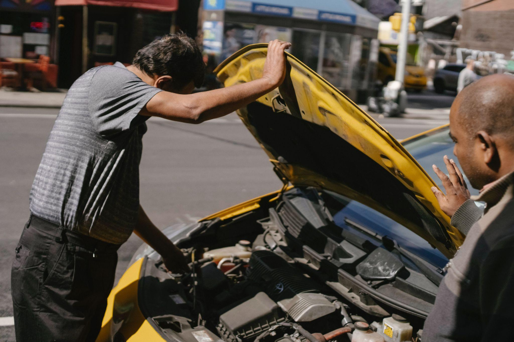 A man trying to repair an old car on the side of the road