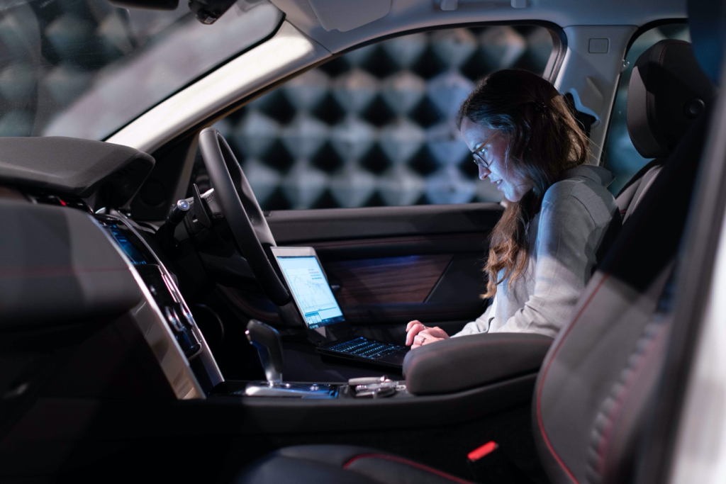 A woman working on her laptop in the car front seat.