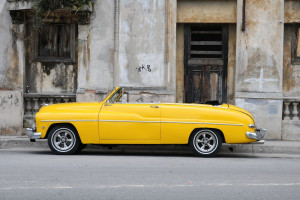 A yellow vintage car parked outside a distressed building.