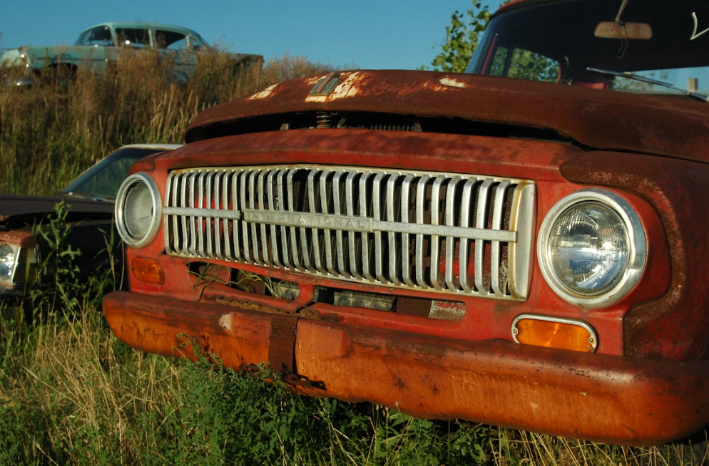 Rusted scrap car in a field.