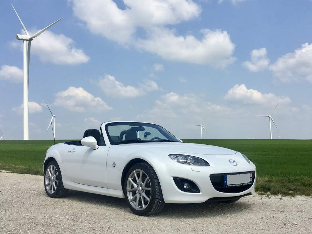 A photo showing a silver car parked near a grassy field.