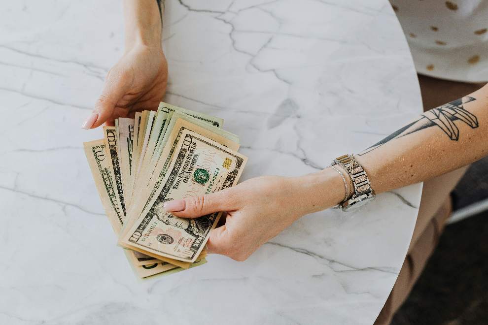 Person with tattoos holding dollar bills in their hands