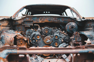 Front view of a junk car without a hood and the rusted engine and parts showing.