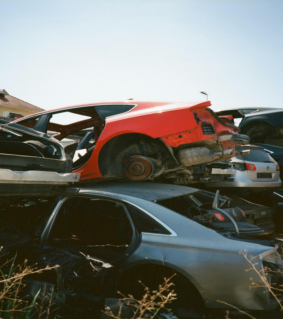 A red car piled on top of a silver one in a car junkyard.